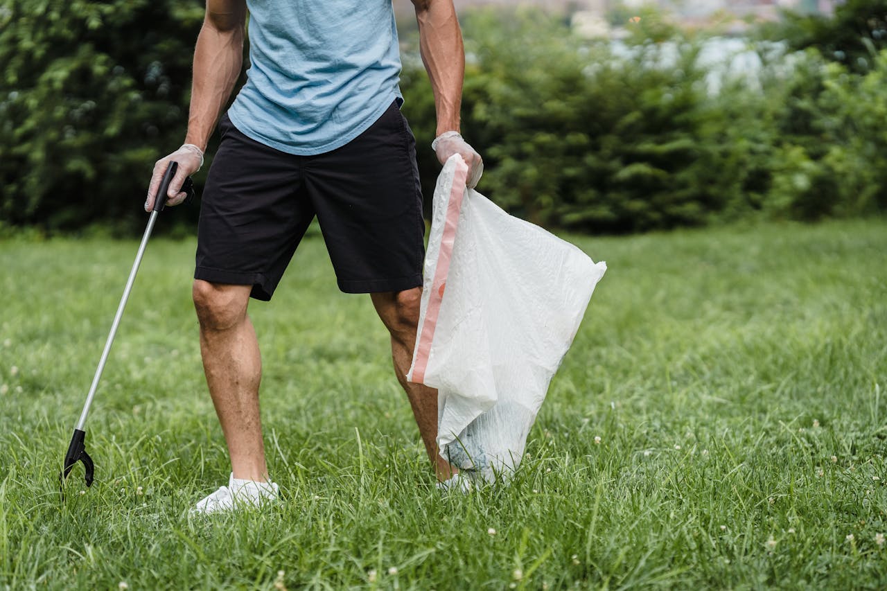Home A volunteer cleaning a park, holding a grabber and garbage bag, promoting environmental well-being.